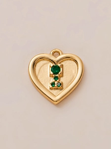 Detail van 18K vergulde hartvormige hanger met groene edelstenen en centraal motief