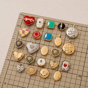 Assorted vintage heart and geometric 18K gold plated pendants displayed on a grid board