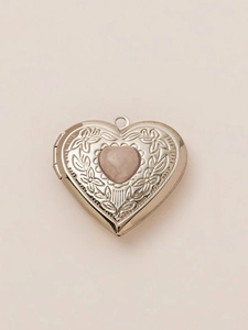 Silver flower engraved heart locket pendant with pink stone on light beige background