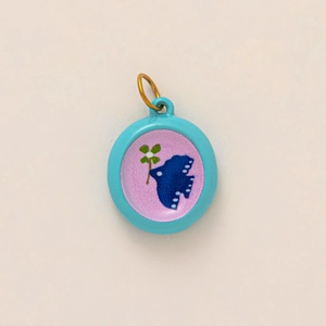 Detail of 18k gold plated round charm featuring butterfly and clover motif in blue enamel