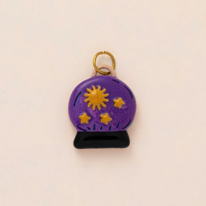 Detail of purple crystal ball charm with sun and star patterns and gold jump ring