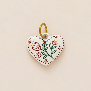 Dettaglio macro di un ciondolo in ceramica a forma di cuore con motivi floreali rossi