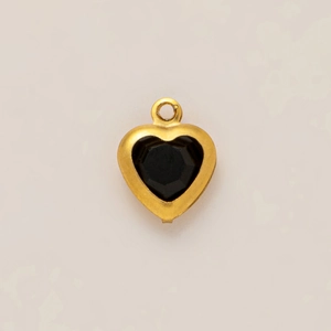 Detail view of heart-shaped gold pendant with central black gemstone inlay on light surface