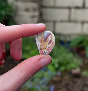 Vue macro d'un petit pendentif lapin en céramique tenu entre deux doigts délicatement