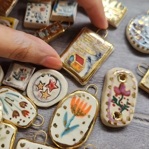 Close-up view of various handmade-style floral printed ceramic pendants with gold plated edges