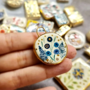 Macro shot of a handmade 18K gold-plated floral charm with blue patterns and gold dots