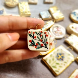 Macro shot of square ceramic flower pendant with 18K gold plated rim and floral pattern