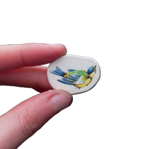 Vue à la main d'un mini pendentif ovale en céramique avec motif d'oiseau coloré sur blanc