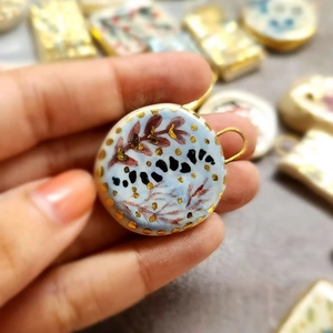 Detail view of a 18K gold plated ceramic flower pendant held to show handmade art