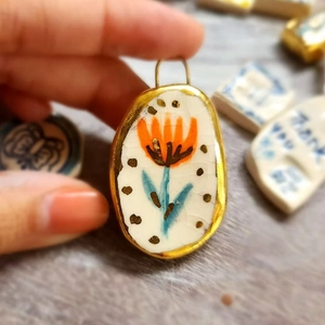 Macro detail of handmade floral ceramic pendant with 18K gold plated edge and top loop