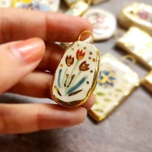 Detail of hand-painted floral ceramic pendant with gold-plated metal edges and ring
