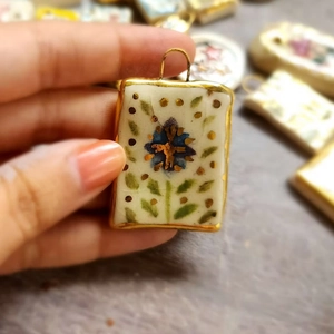 Detailed macro of a 18K gold plated ceramic floral pendant with hand-painted patterns
