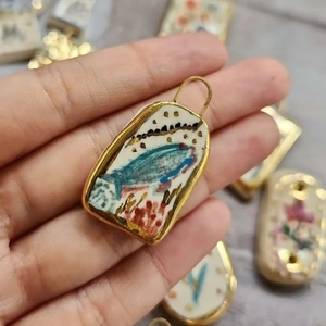 Macro detail of hand-painted floral ceramic pendant with 18K gold-plated edge and ring
