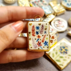 Macro view of rectangular 18K gold plated pendant with floral hand-painted enamel detail