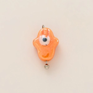 Macro shot of orange ceramic Hamsa pendant with evil eye and 18K gold-plated hook