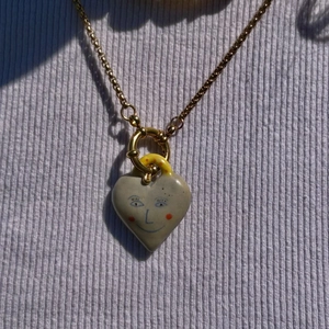 Gros plan du pendentif cœur en céramique grise avec dessin de visage sur chaîne en or 18K