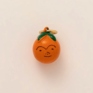Vue détaillée d'une breloque orange en émail avec un visage mignon et une feuille verte