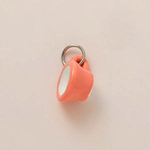 Macro detail of a 3D miniature ceramic coffee cup pendant in coral pink with white glaze