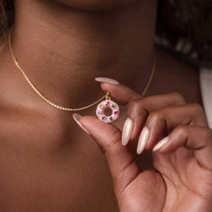 Detail of a pink enamel donut pendant necklace with multi-color baguette gemstones