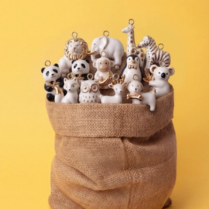 Set of 12 white ceramic animal pendants with 14K gold accents in a rustic burlap bag