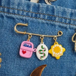 Broche de imperdible dorado con colgantes de esmalte sobre fondo de tela vaquera