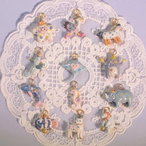 Set of 12 animal-themed enamel pendants with gold rings on a white lace coaster