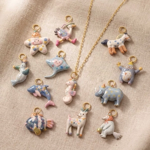 Colorful animal enamel pendants with gold rings on beige linen background