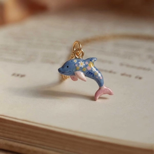 Macro detail of a dolphin pendant with floral enamel patterns on vintage book pages