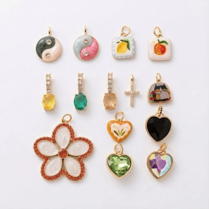 Flat lay of diverse gold-plated charms including yin-yang, fruits, and colorful hearts