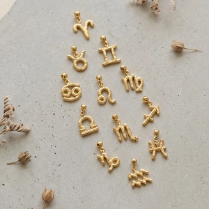 Golden zodiac pendant set with hammered texture on a minimalist stone background