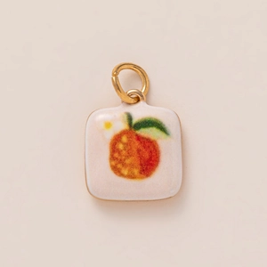 Detail view of square white enamel charm featuring hand-painted orange fruit with gold loop