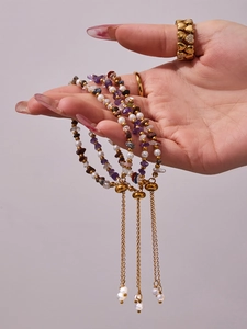 Close-up of pearl and purple stone beaded bracelets with long gold chain tassels and rings