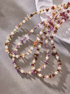 Detailed shot of gold-plated beads, pearls, and colorful natural stones on steel chains