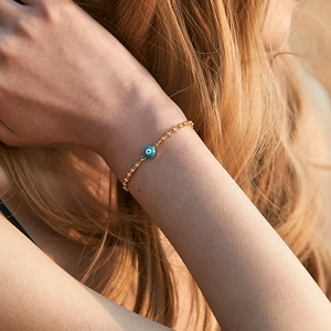 Golden bead chain bracelet featuring a blue evil eye lucky charm on a model's wrist