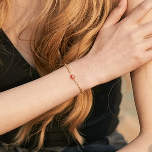 Minimalist 18K gold plated beaded bracelet with a red evil eye charm on model wrist