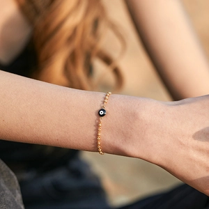 Primer plano de pulsera de cuentas doradas con colgante de ojo turco azul en la muñeca