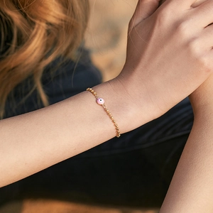 Detalle del amuleto rosa del ojo turco en una pulsera de cuentas doradas para mujer