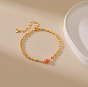 Detalle de pulsera de cuentas doradas con amuleto de ojo turco rojo y cierre de mosquetón