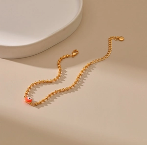 Detalle de pulsera de cuentas doradas con dije de ojo turco naranja y cierre de langosta