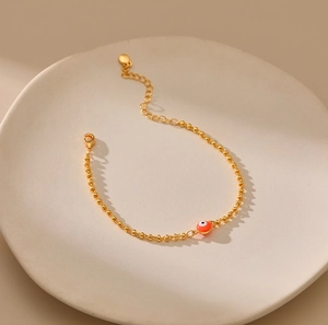 Detalle de pulsera de cuentas doradas con dije de Ojo Turco rojo y cierre de langosta