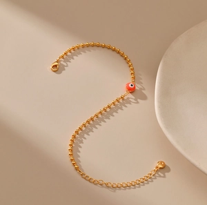 Detalle de pulsera de cuentas doradas con ojo turco rojo y cierre de langosta ajustable