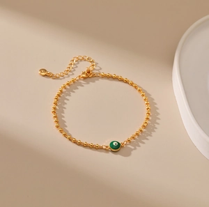 Detalle de pulsera de cuentas doradas con colgante de ojo turco verde y cierre de langosta
