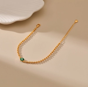 Detalle de pulsera de cuentas doradas con amuleto de ojo turco verde y cierre de mosquetón