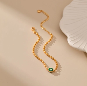 Detalle de pulsera de cuentas doradas con colgante de ojo turco verde esmaltado y cierre de mosquetón