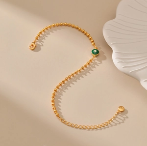 Detalle de la pulsera de cuentas doradas con colgante de ojo turco verde y cierre de mosquetón
