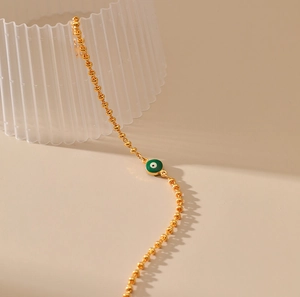 Detalle de pulsera de cuentas doradas con un dije de ojo turco en esmalte verde vibrante