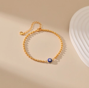 Detalle de pulsera de cuentas doradas con amuleto de ojo turco azul y cierre ajustable