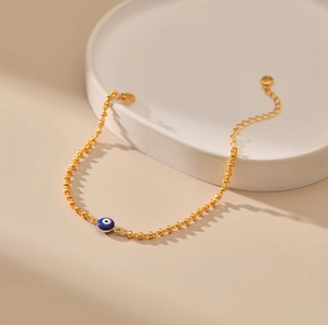 Detalle macro de pulsera de cuentas doradas con dije de ojo azul sobre bandeja blanca
