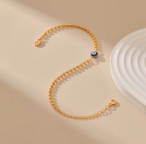 Detalle de pulsera de cuentas doradas con ojo turco azul esmaltado y cierre de mosquetón