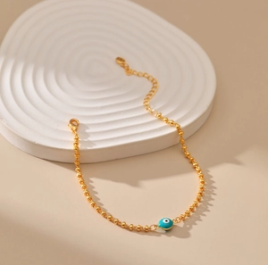 Detalle de pulsera de cuentas doradas con dije de ojo turco azul y cadena ajustable